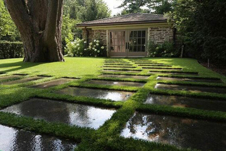 Modern backyard with synthetic grass path between dark stone pavers reflecting surrounding trees.